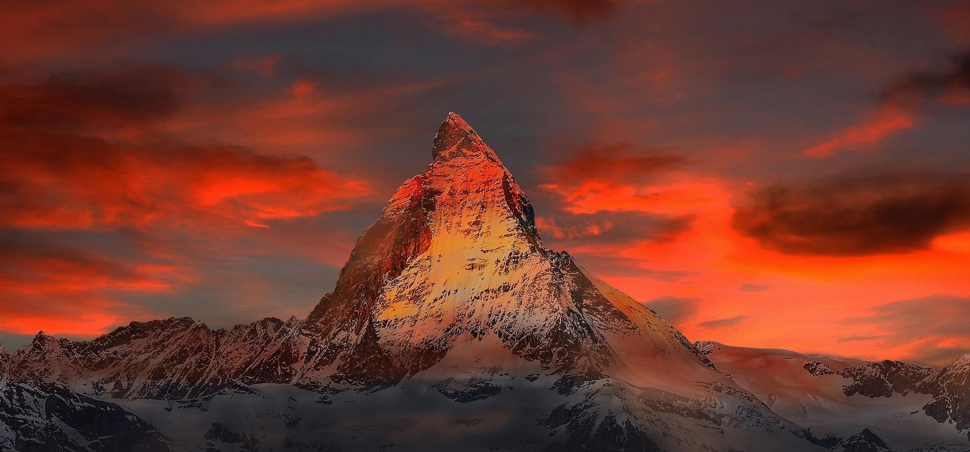 A sharply pointed mountain appears red and yellow in a deeply coloured sunset (switzerland)