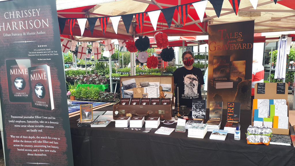 Chrissey's stall at the Newark Book Festival Literature Village. Black, white and red bunting, roller banners, copies of Mime in a vintage suitcase surrounded by occult items.